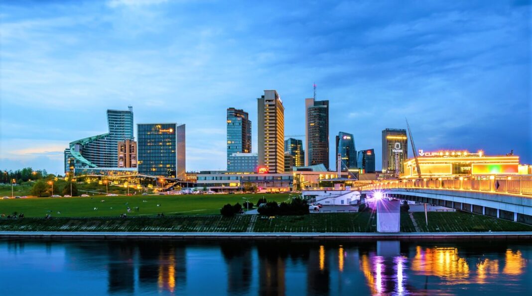 Didžiausi Lietuvos miestai: Vilniaus modernusis rajonas su apšviestais dangoraižiais ir Neries upe.