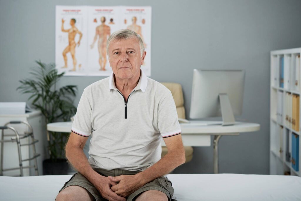 Kraujas išmatose reikalauja medicininės apžiūros – vyresnio amžiaus vyras sėdi gydytojo kabinete, laukdamas konsultacijos.