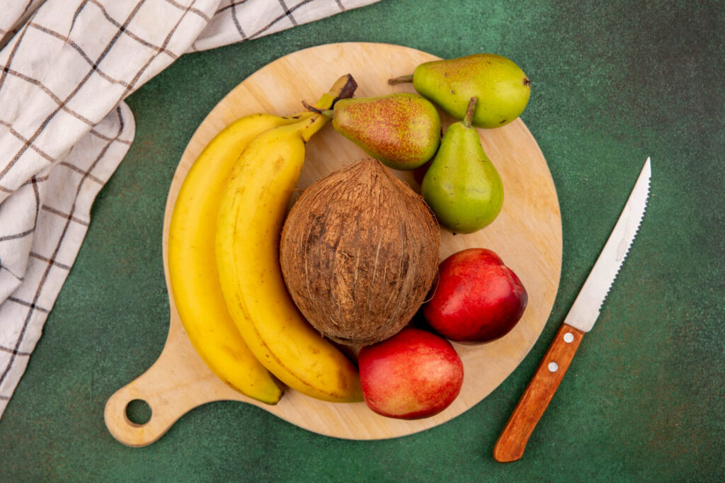 Bananai, kriaušės ir kokosas ant medinės lentelės.