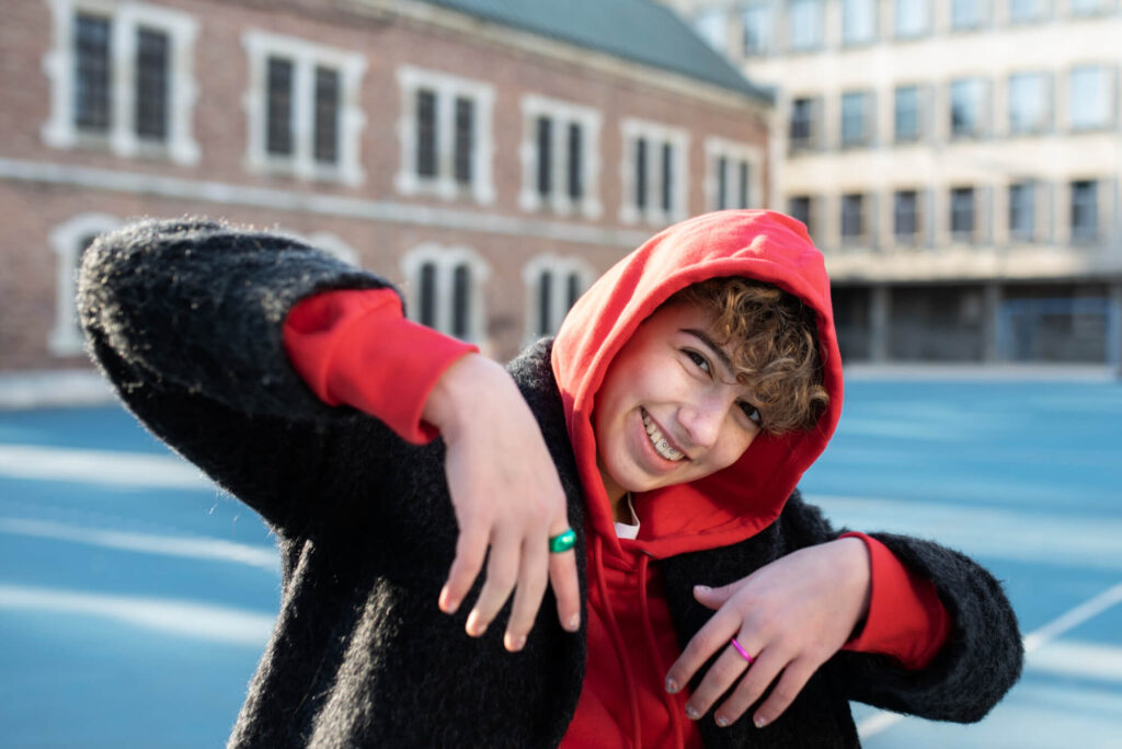 Ką reiškia sigma – paauglys su raudonu džemperiu ir garbanotais plaukais šypsosi lauke.