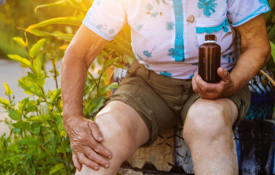 Greita pagalba sąnariams – vyresnio amžiaus moteris masažuoja skaudamą kelį su natūraliu tepalu