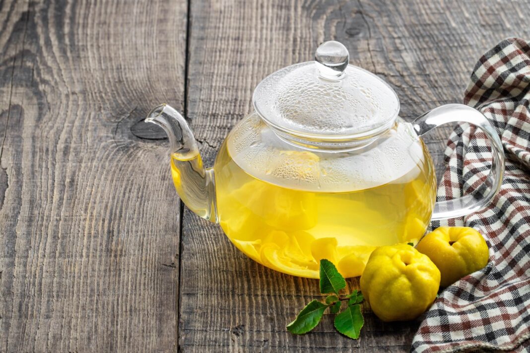 Svarainių arbata stiklo arbatinuke, padėta ant medinio stalo su svarainiais.