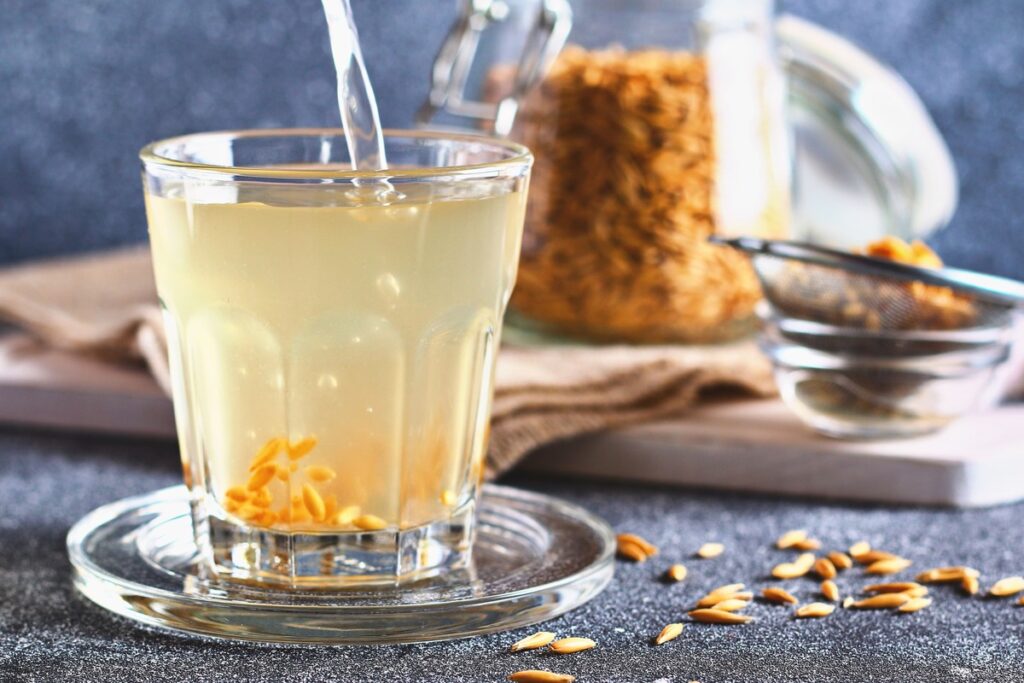 Avižų vanduo cholesteroliui – natūralus gėrimas stiklinėje, šalia avižų grūdai.