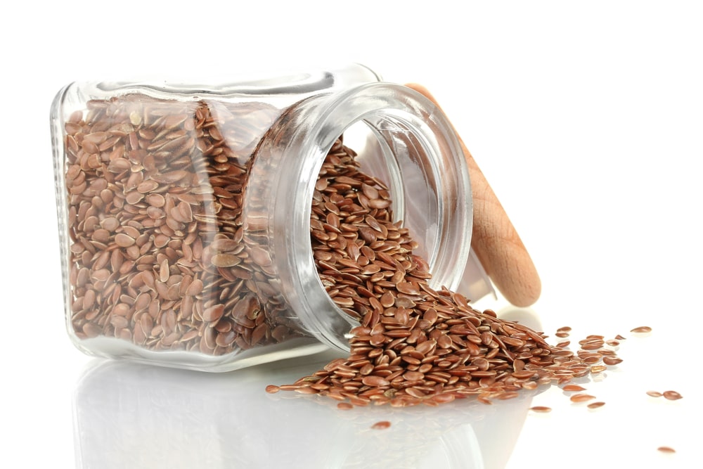 Linų sėmenys nuo refliukso stiklainyje ant balto paviršiaus