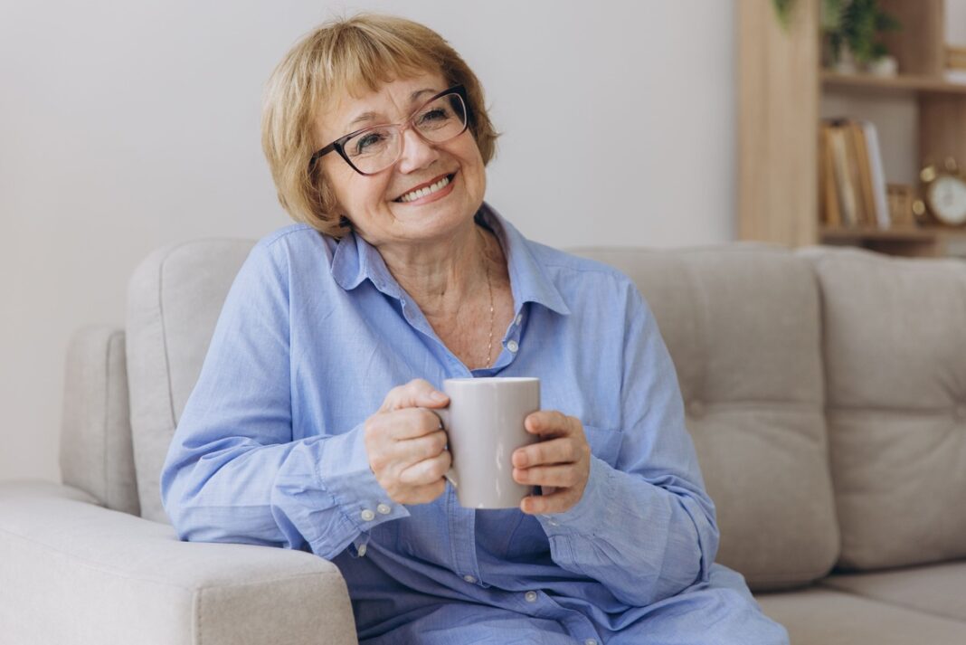 Arbata nuo kojų tinimo – laiminga moteris su puodeliu arbatos, sėdinti ant sofos ir jaučianti palengvėjimą po natūralaus gydymo.