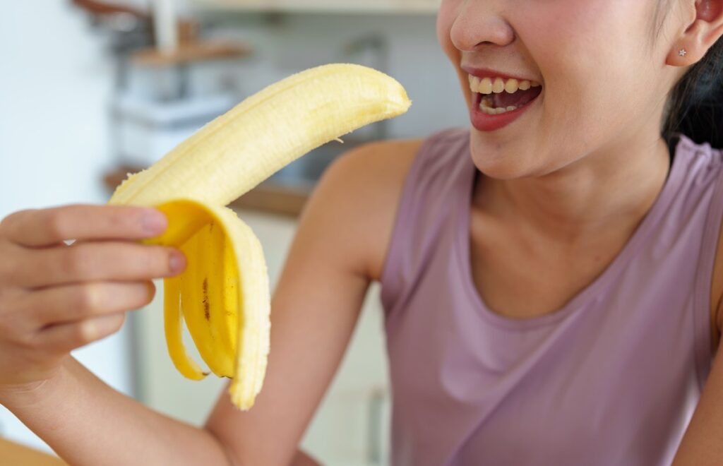 Bananai ir svorio metimas – moteris valgo šviežią bananą po treniruotės, pasirinkusi sveiką užkandį lieknėjimui.