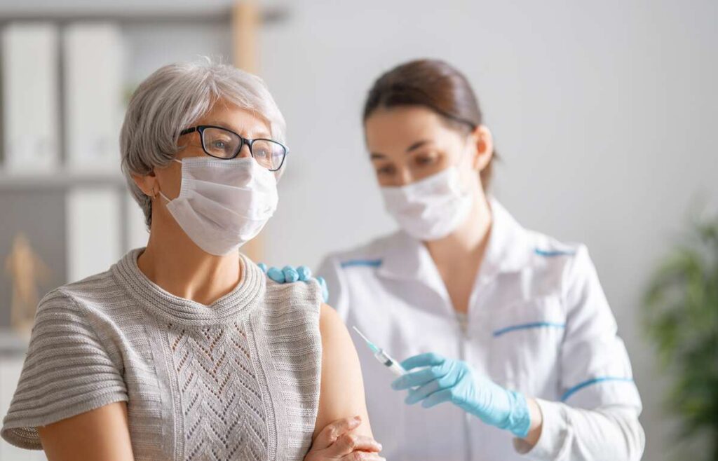 Covid atmaina Stratus – moteris su apsaugine kauke skiepijama nuo kvėpavimo takų infekcijų gydymo įstaigoje.