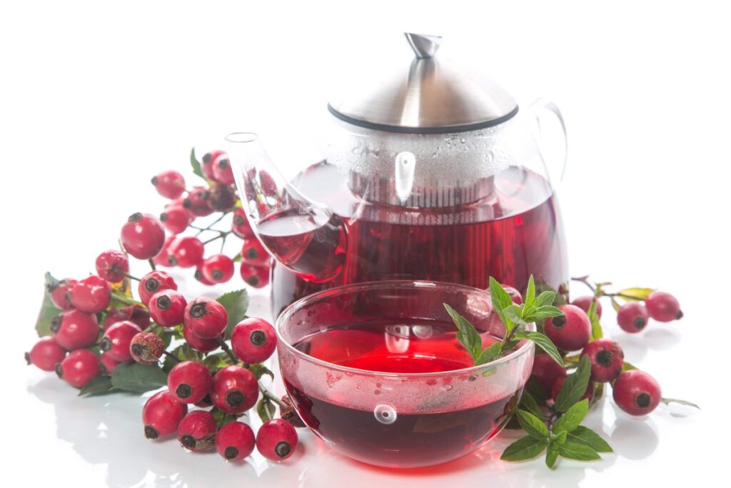 Gėrimas kraujagyslėms valyti su erškėtuogių arbata – puodelis raudono užpilo šalia stiklinės arbatinuko ir šviežių uogų.