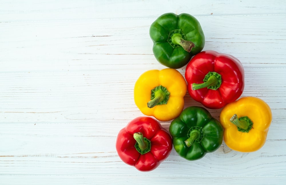 Kuri paprika sveikiausia – žalių, geltonų ir raudonų paprikų kompozicija ant medinio stalo, atskleidžianti spalvų skirtumus.