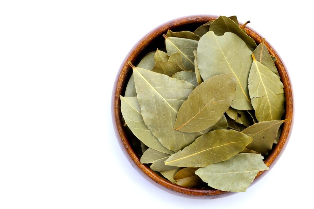 Lauro lapas kojinėse – džiovinti lapai keraminiame dubenėlyje baltame fone.