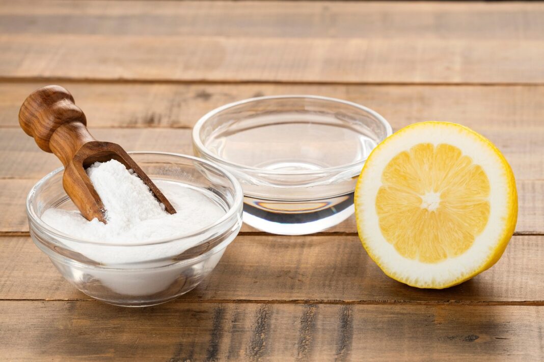 Natūralus mišinys inkstų akmenims: stiklinis indelis su soda, citrinos puselė ir vanduo ant medinio stalo.