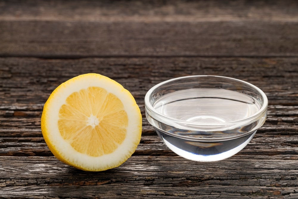Natūralus mišinys inkstų akmenims: stiklinis indelis su aliejumi ir citrinos puselė ant tamsaus medinio paviršiaus.