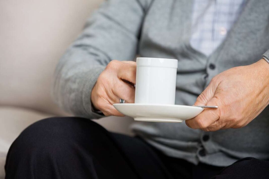 Sąnarių skausmo mažinimas – vyresnio amžiaus žmogus rankose laiko puodelį šilto gėrimo, padedančio palengvinti simptomus.