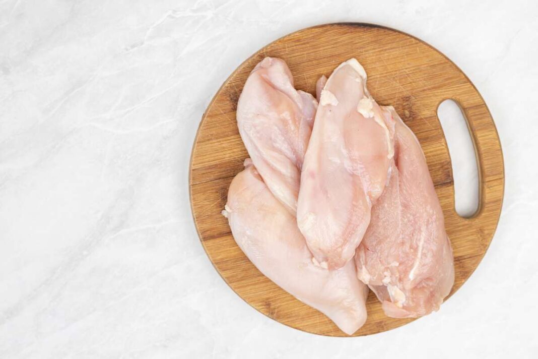 Žalios vištienos krūtinėlės ant medinės lentelės – pavyzdys, kaip balti dryžiai vištienoje atsiranda dėl intensyvaus auginimo.