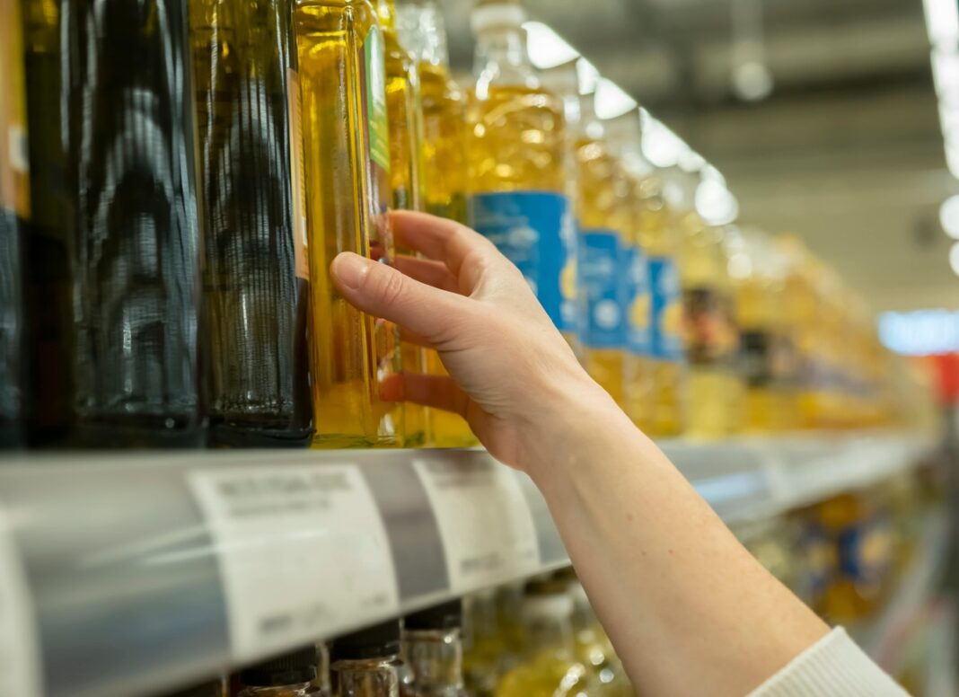 Pirkėjas ranka renkasi augalinį aliejų parduotuvės lentynoje – tarp jų gali būti ir blogiausi aliejai, netinkami kepimui.
