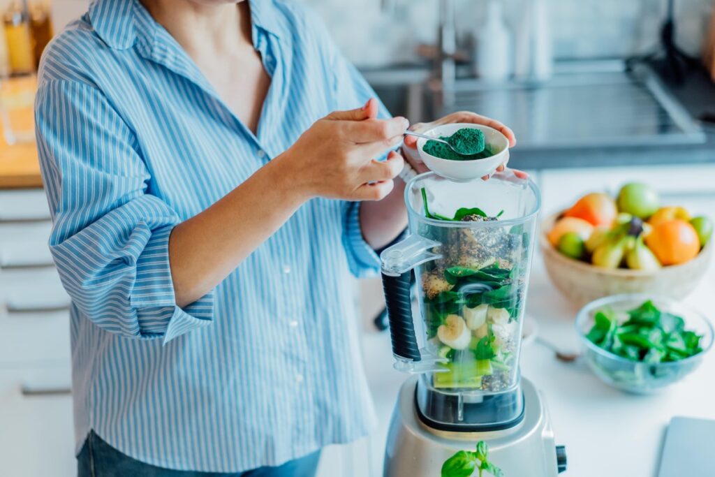 Į virtuvinį trintuvą beriama spirulina kartu su špinatais ir bananais – natūralus receptas kepenų ir kraujo valymui.