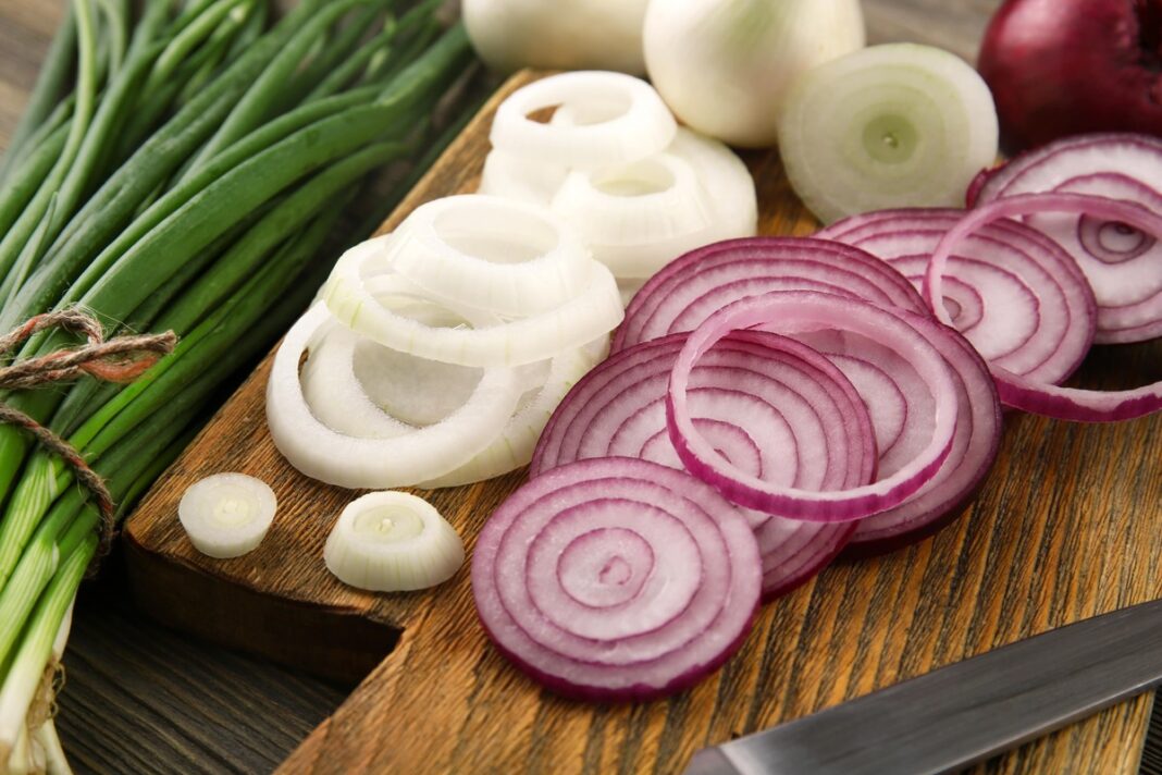 Pjaustyti balti ir raudoni svogūnai su laiškais ant medinės lentelės – natūralus būdas stiprinti sveikatą kiekvieną dieną.