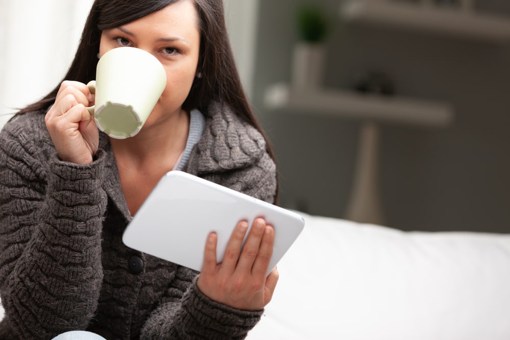 Moteris gurkšnoja vakarinį gėrimą prieš miegą lieknėjimui – ramus laikas su knyga ar planšete.