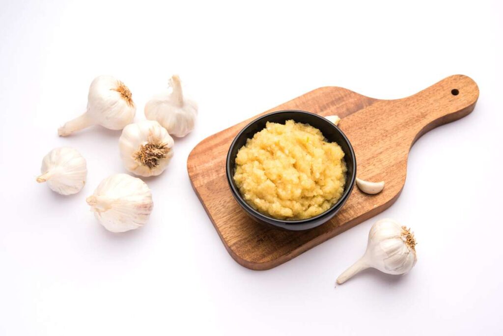 gamtos antibiotikai česnakas pasta dubenėlyje ant medinės lentelės – natūralus sveikatos stiprinimo būdas.