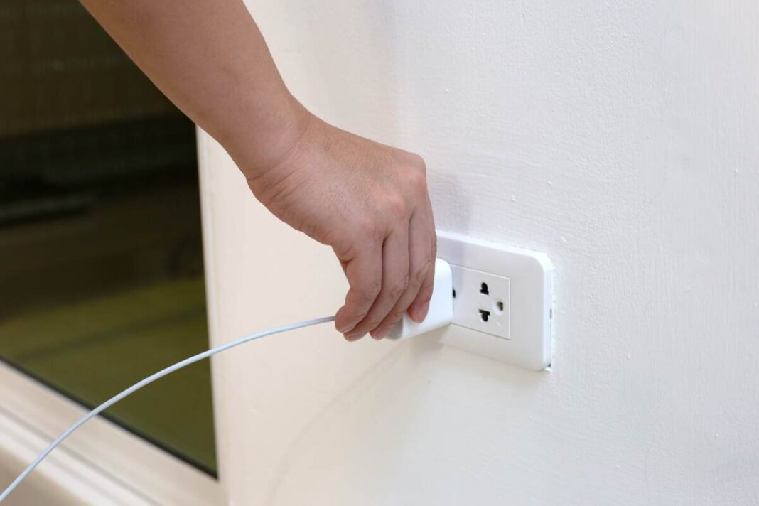 Įkroviklis rozetėje be telefono – žmogus ranka jungia laidą prie sieninio lizdo.