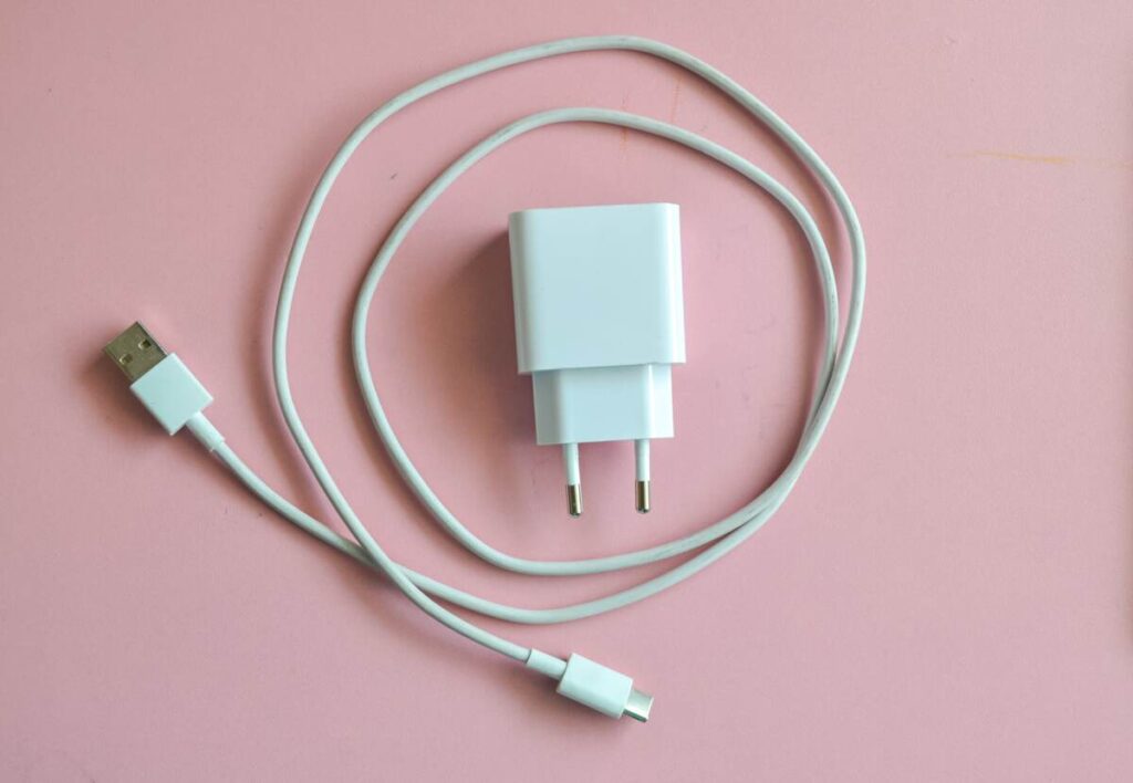 Įkroviklis rozetėje naudojimui paruoštas – baltas USB adapteris su ilgu laidu ant rožinio fono.