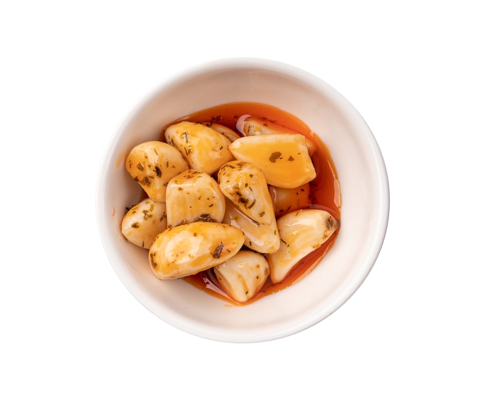 Marinuoti česnakai žiemai baltoje lėkštėje – traškūs, aromatingi ir gardūs, tinkantys žiemos užkandžiams.