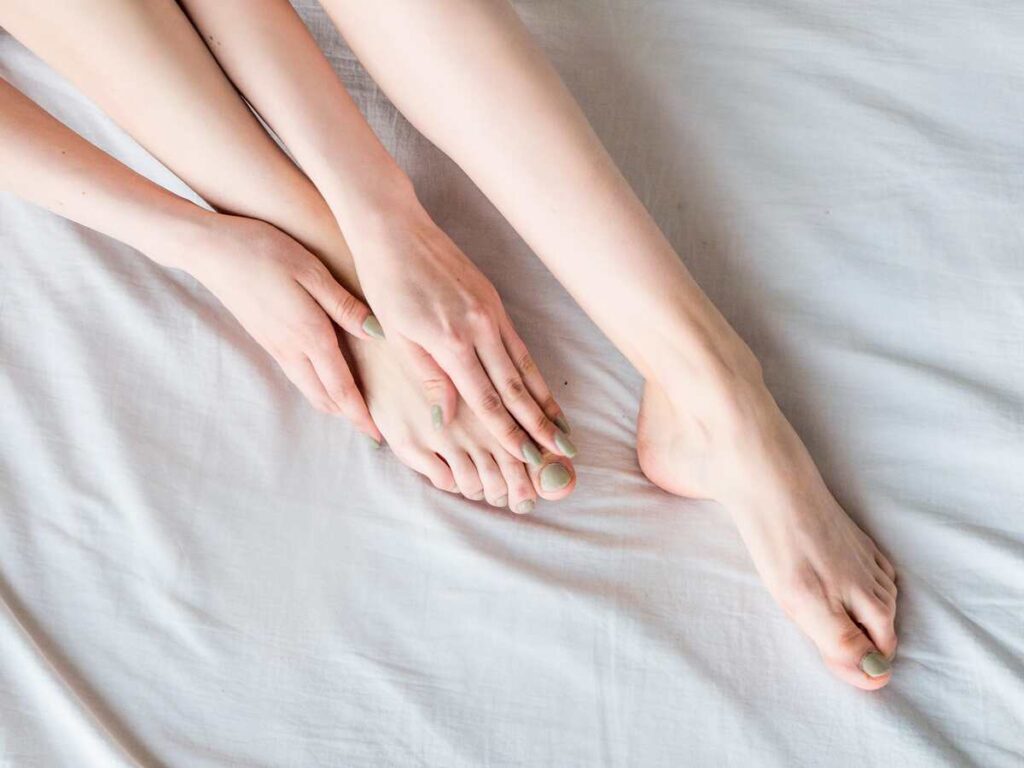 Natūralūs būdai nuo tinimo – moteris masažuoja pėdas, siekdama palengvinti patinimą.