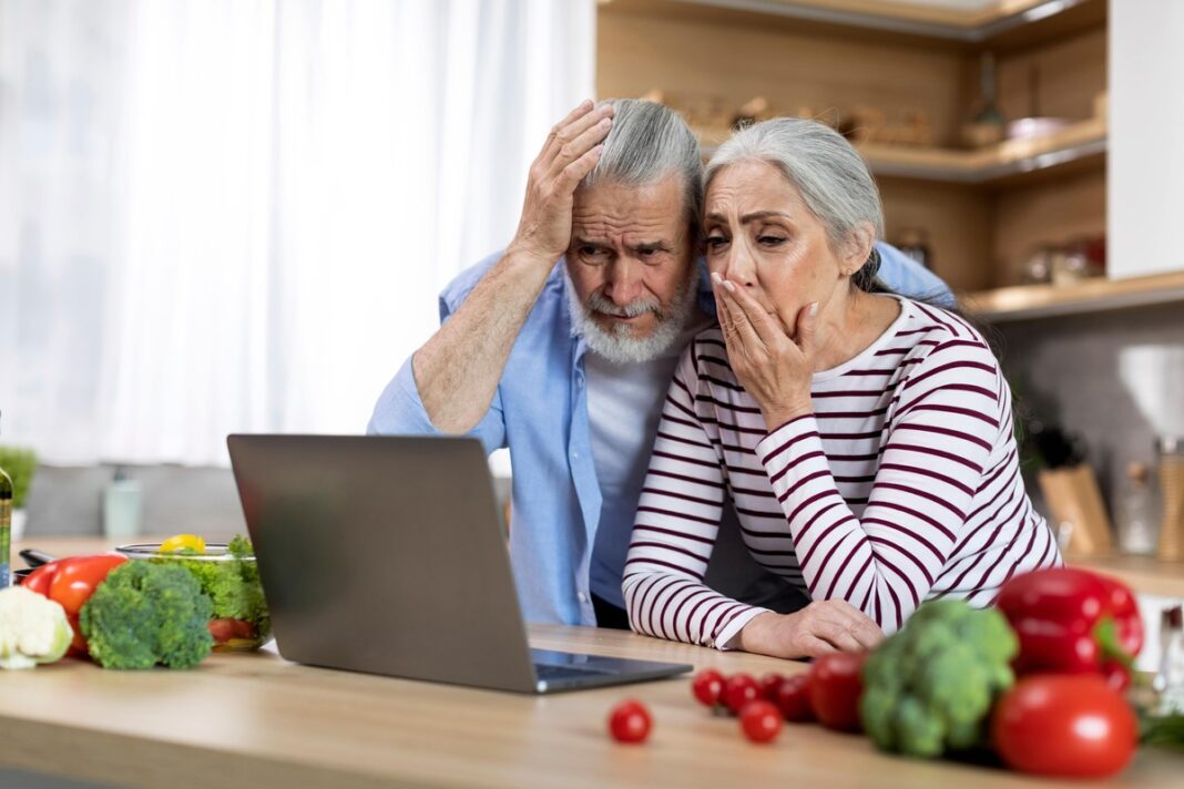 Vyresnė pora nustebę žiūri į kompiuterį, domisi pieno produktų poveikiu po 50 metų.