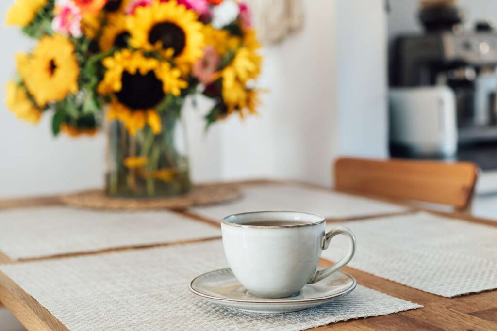 Saulėgrąžų šaknų arbata ant stalo su puodeliu ir saulėgrąžų vaza fone.