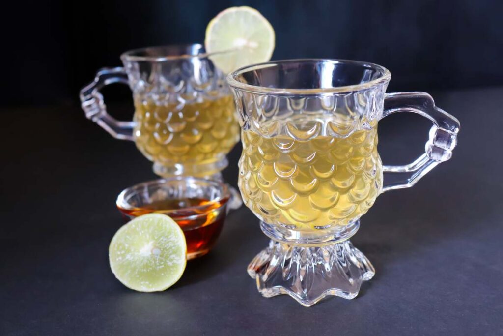 Vaistažolės svorio metimui – imbiero ir citrinos gėrimas stiklinėse taurėse su šaukšteliu medaus.