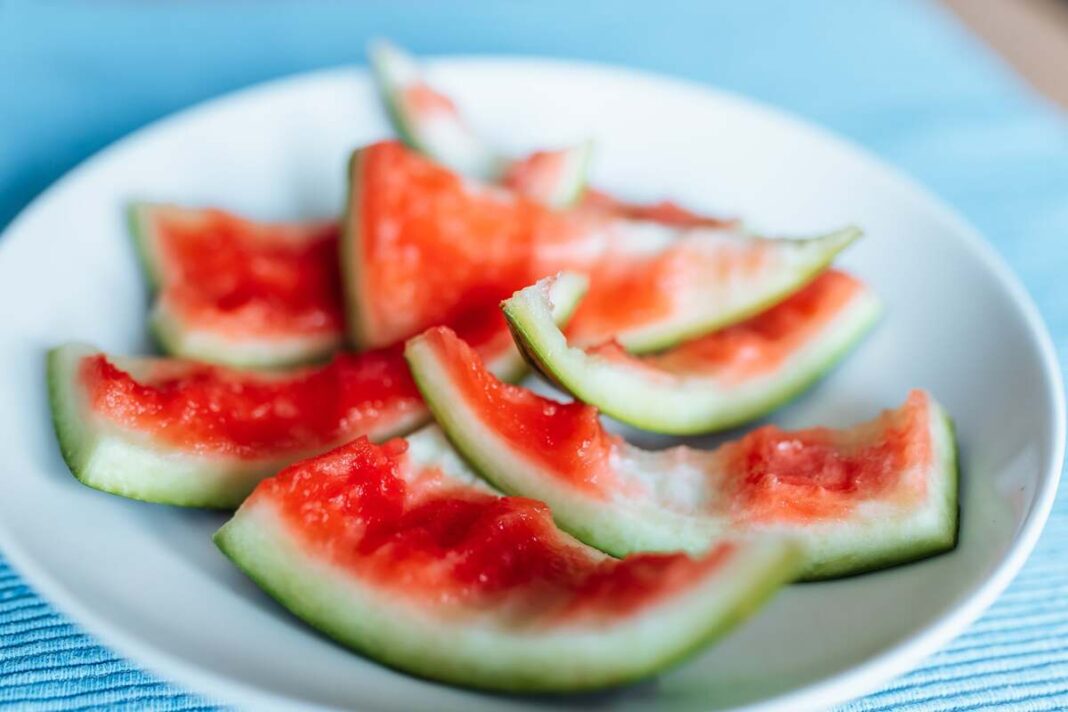 Arbūzų žievelių nauda sveikatai ir organizmui – suvalgyto arbūzo žievelės baltame dubenyje ant mėlyno stalo.