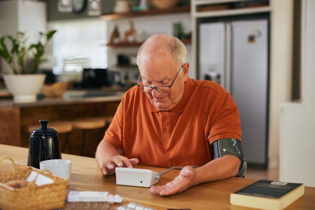 Cholesterolis ir jo priežastys – vyras namuose matuoja kraujospūdį ir stebi sveikatos pokyčius.