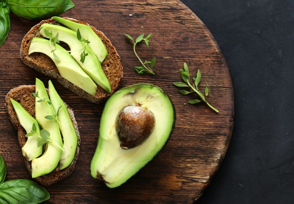 Cholesterolis krenta greitai valgant avokadą – riekės su avokadu ir žolelėmis ant medinės lentelės.