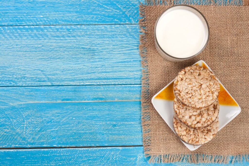 Grikiai su kefyru svoriui – stiklinė kefyro su trapučiais ant stalo, tinkama sveikai mitybai ir svorio mažinimui.