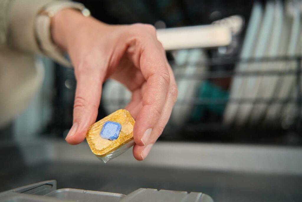 Indaplovės tablečių naudojimas namams – tabletė laikoma rankose prieš įdedant į indaplovę, parodant universalų jos pritaikymą.