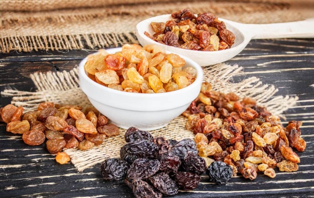 kepenų valymas razinomis – įvairių atspalvių džiovintos razinos baltuose dubenėliuose ant medinio stalo.