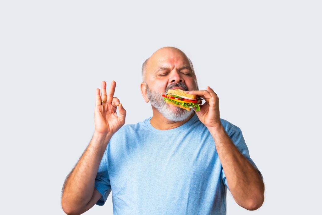 maistas gerai nuotaikai vaizduojamas per vyresnį vyrą, kuris mėgaujasi skaniu sumuštiniu ir gera emocija.