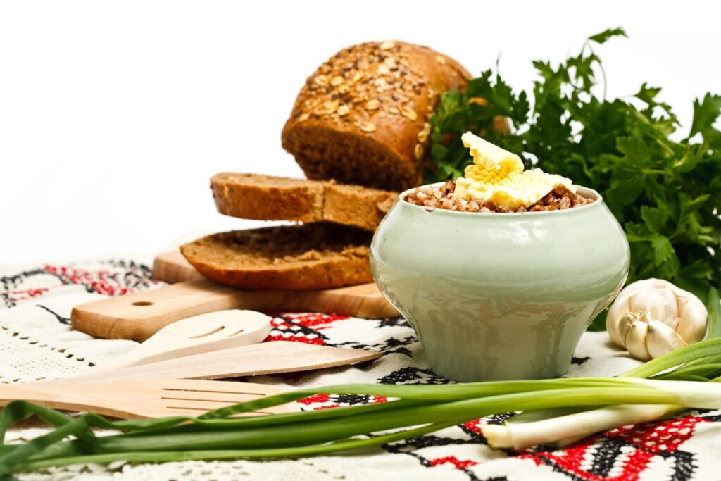 Produktai kasai – dubenėlyje patiekti grikiai su sviestu, šalia žalumynai ir pilno grūdo duona.