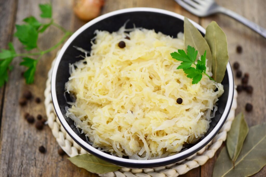 raugintų kopūstų poveikis – dubuo su raugintais kopūstais, pagardintais lauro lapais ir pipirais ant medinio stalo.