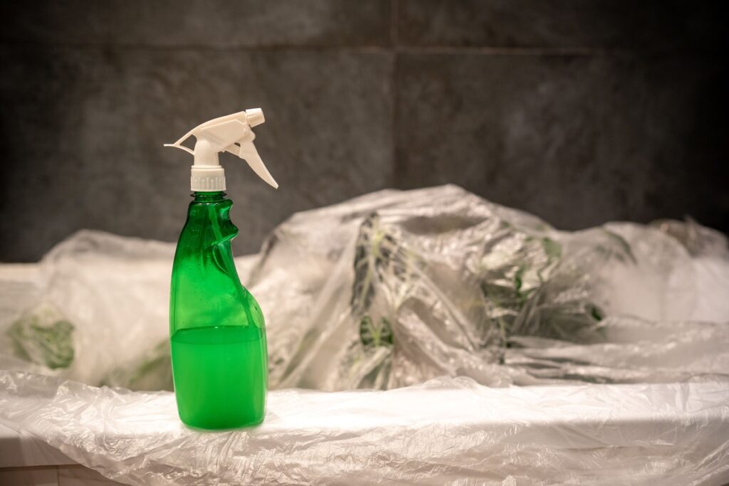 Šiltnamio dezinfekavimas purkštuvu – žalias butelis su tirpalu ant plastiko plėvelės, pasiruošimas valymui.