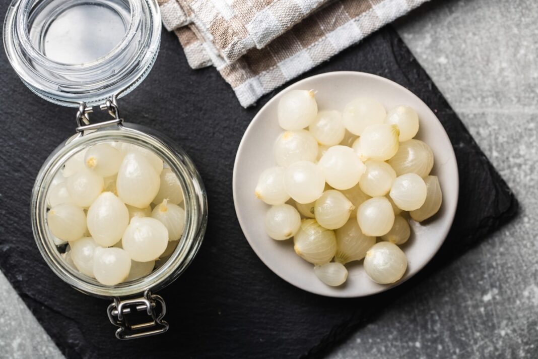 svogūnų konservavimas – maži svogūnai uždaryti stiklainyje ir patiekti lėkštėje ant tamsaus paviršiaus.