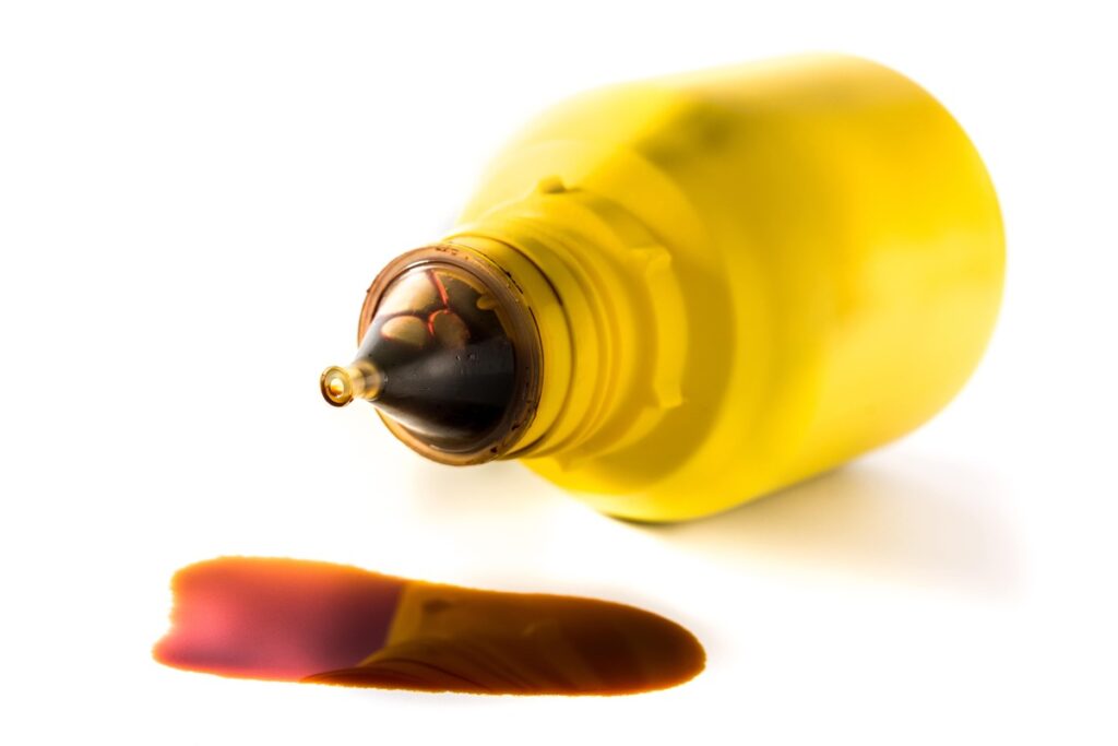 Vienas lašas jodo – plastikinis buteliukas su rudai oranžiniu tirpalu, iš kurio išbėgęs nedidelis lašas.