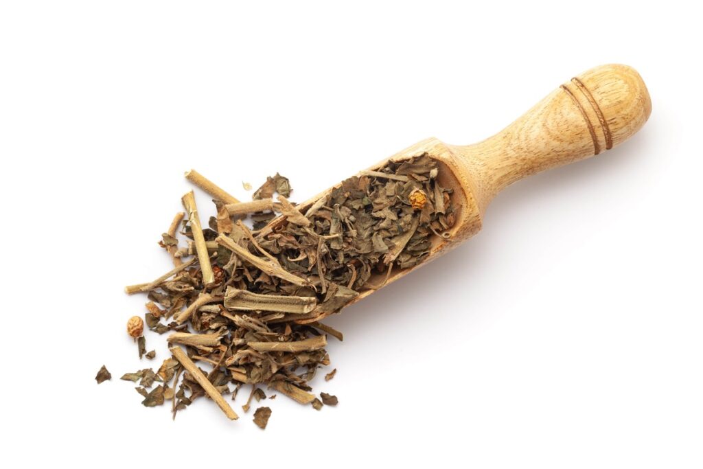 Ašvaganda nervams ir miegui – džiovintos šaknys ir lapai medinėje samtelėje baltame fone.