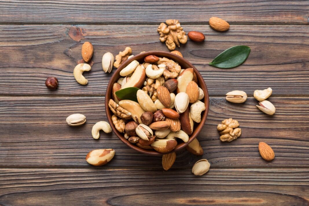 Aukštas kreatininas – maistinga įvairių riešutų mišinio porcija moliniame dubenėlyje ant medinio stalo.