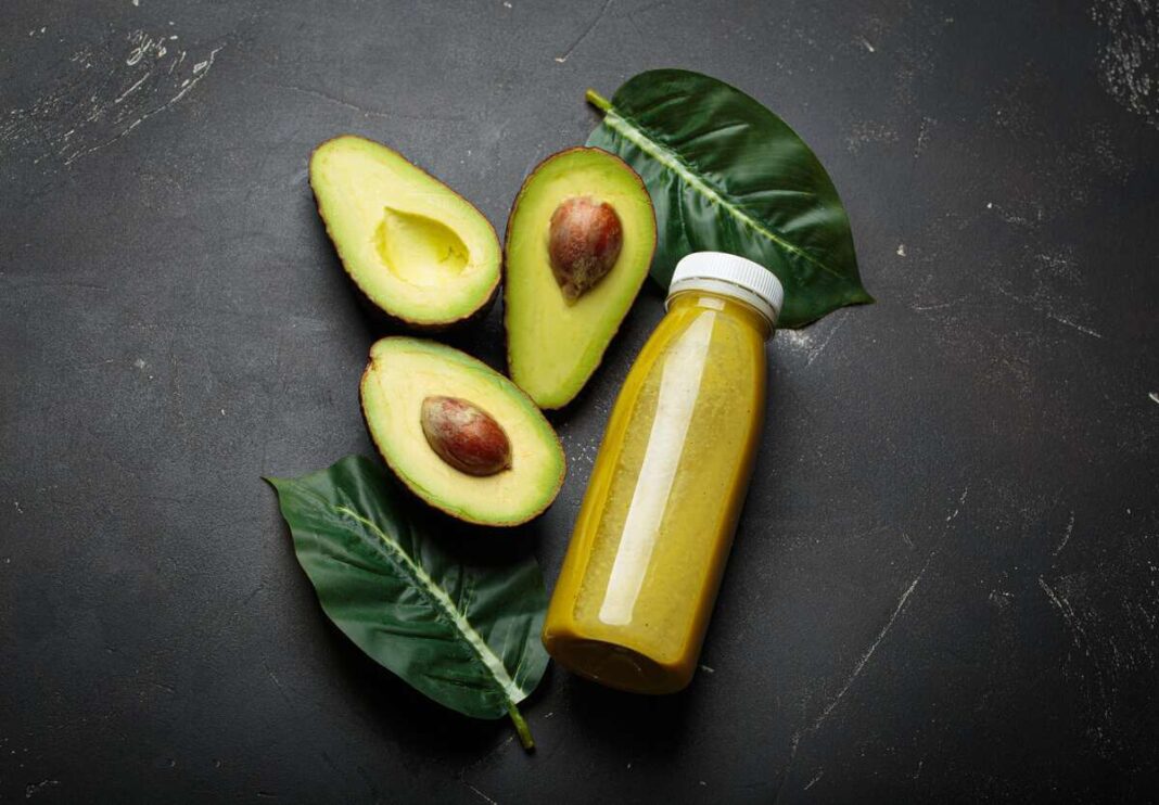 avokado sėklos gėrimas – avokado puselės ir skaidrus buteliukas su tirštu žaliu gėrimu