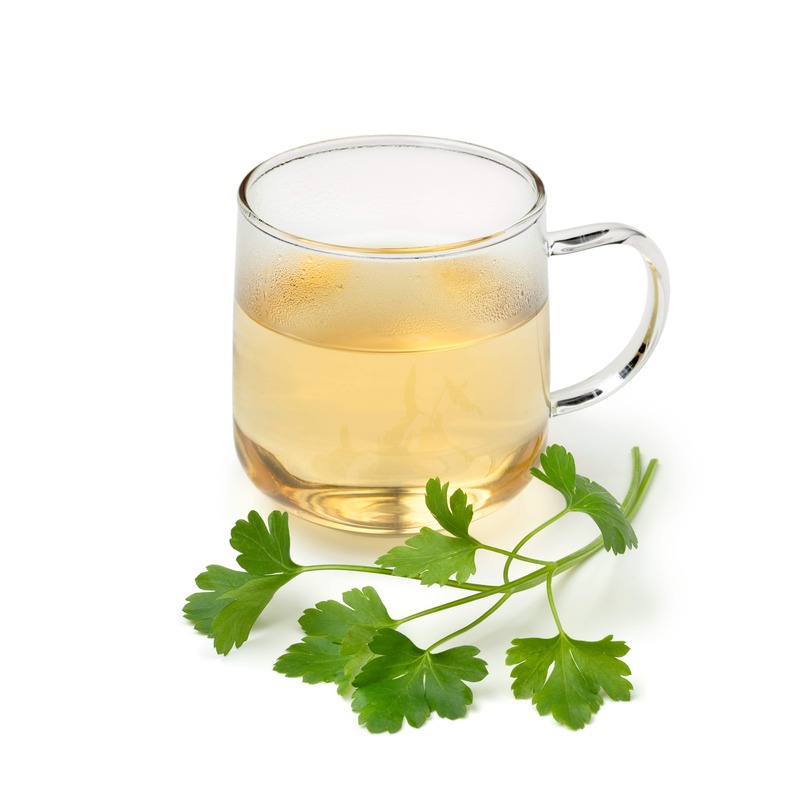 gėrimas nuo skysčių susilaikymo – stiklinė petražolių arbatos su šviežiomis žolelėmis ant balto fono.