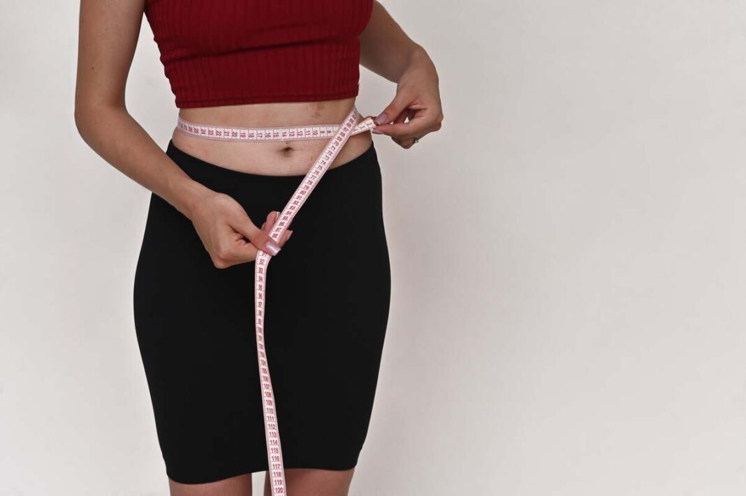 Kokosų aliejus svorio metimui – moteris matuojasi liemens apimtį po svorio mažinimo.