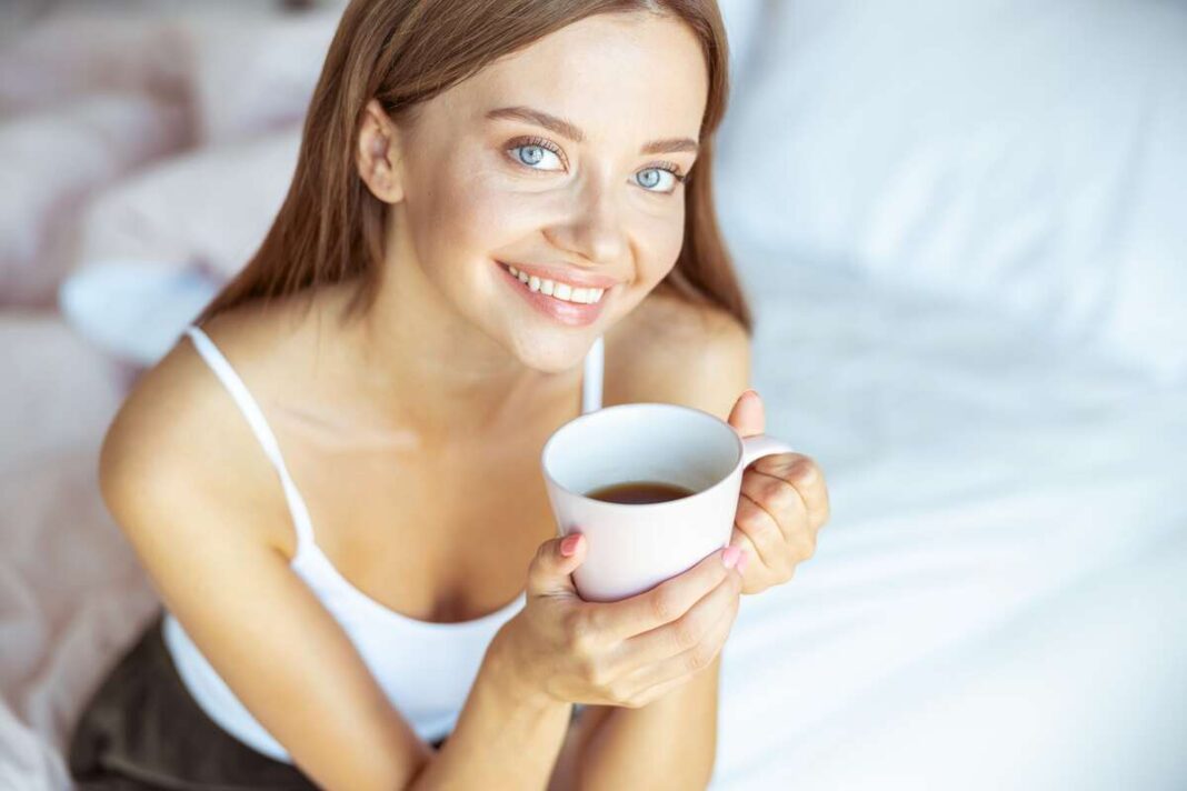 Mišinys prieš miegą – moteris su puodeliu gėrimo atrodo pailsėjusi ir rami.