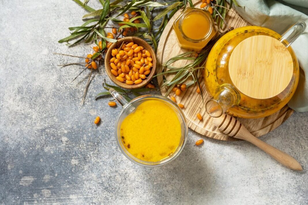 Šaltalankių vartojimas – šaltalankių arbata ir sultys su medumi ant stalo.