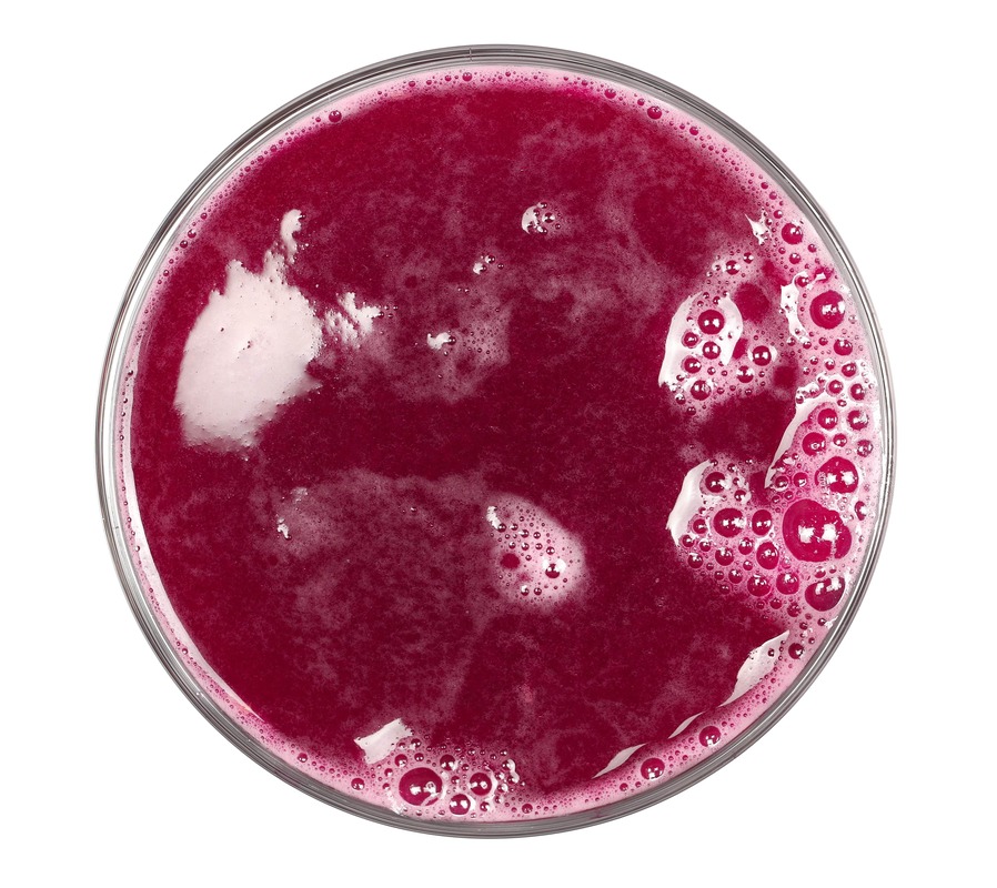 Spanguolių gėrimas nuo cistito – ryškiai raudonos sultys stikliniame inde, vaizdas iš viršaus.